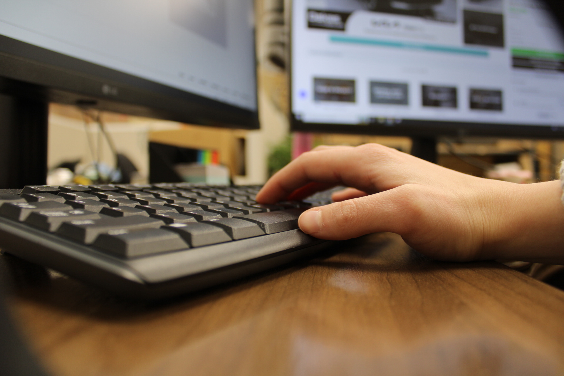 A hand on keyboards at a desk looking at the Oakes website.